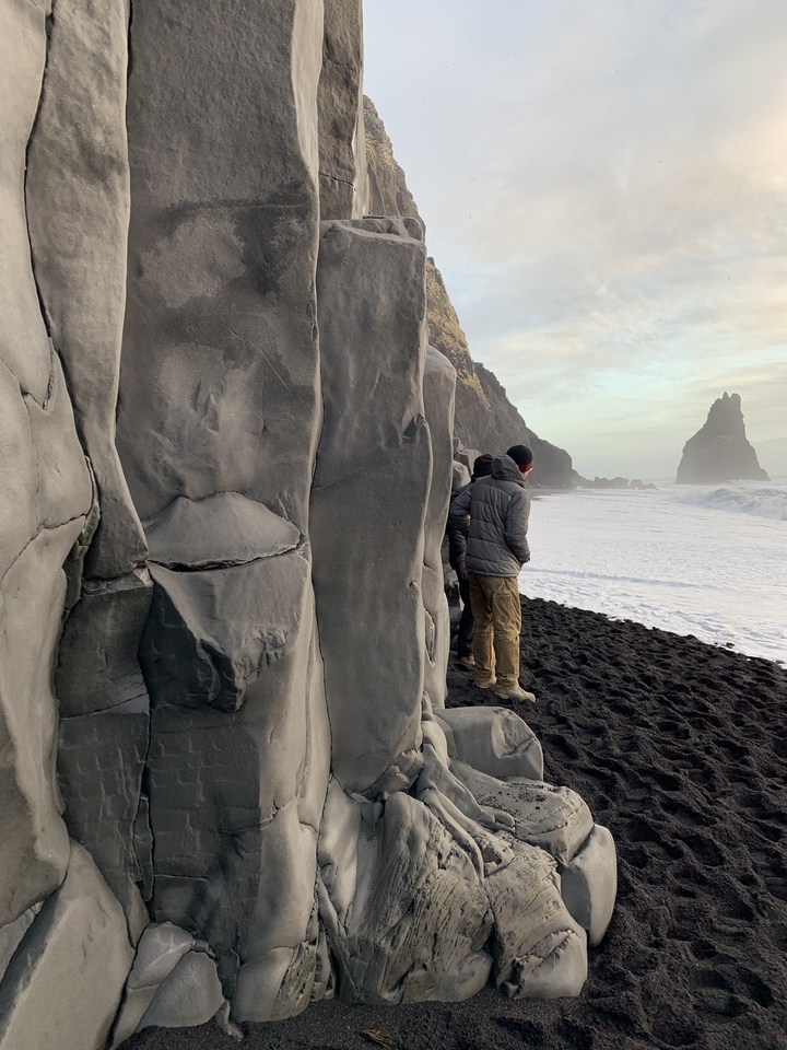 People standing near a rocky beach with sea stacks in the background.