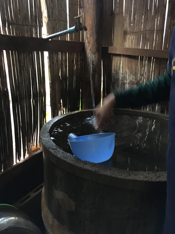 Personne utilisant une cuillère bleue dans un bassin d'eau à l'intérieur d'une hutte.