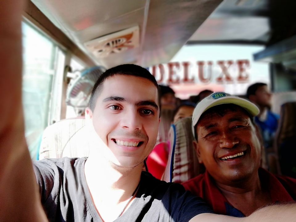 Deux hommes souriants dans un bus avec un panneau 'Deluxe' au-dessus d'eux.