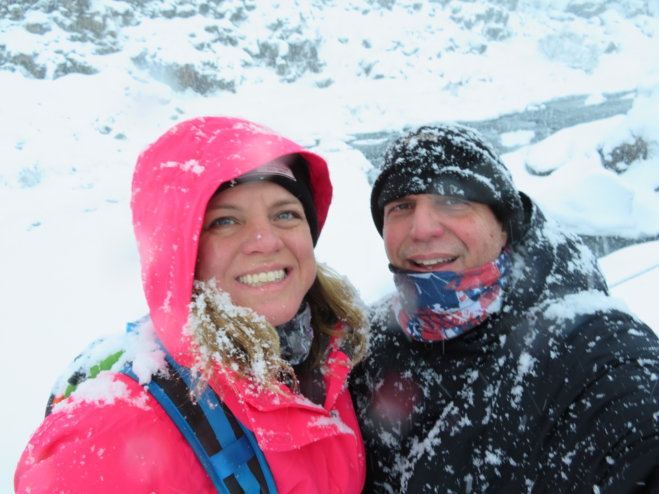 Deux personnes en équipement de neige souriant avec de la neige qui tombe.