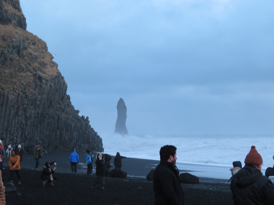 Des touristes se promènent le long d'une plage noire avec Reynisdrangar en arrière-plan.
