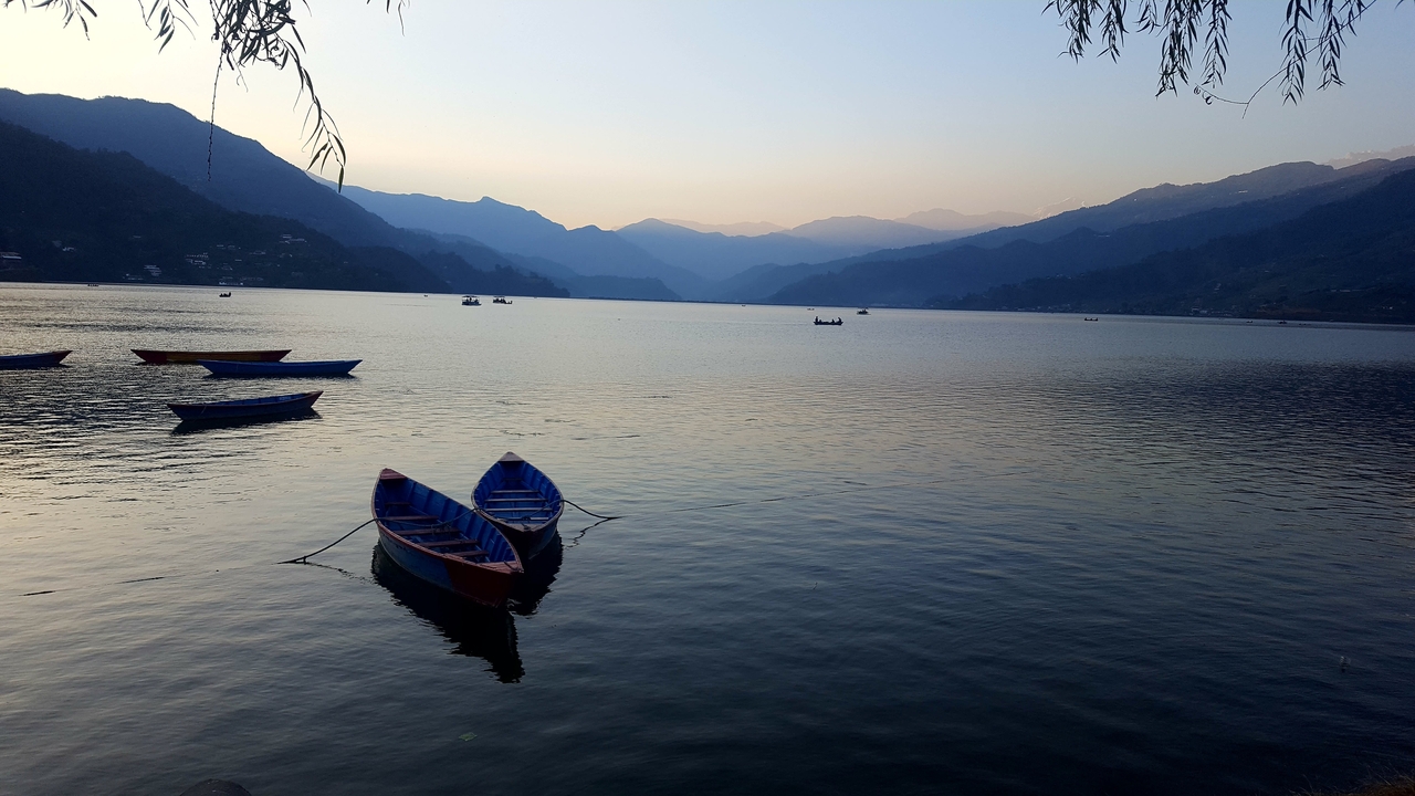 Vue sereine d'un grand lac avec de petits bateaux et un arrière-plan montagneux au crépuscule.