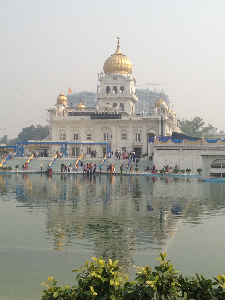 Sikh temple with people gathered around and a reflection in water.