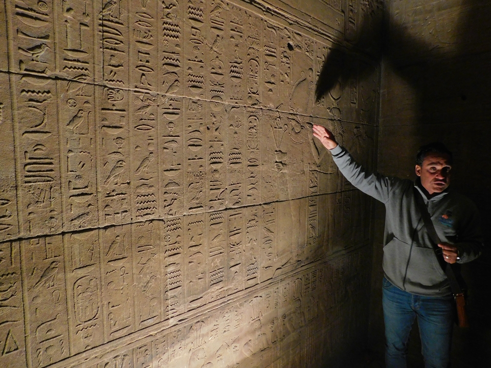 Un guide expliquant les hiéroglyphes sur le mur d'un temple de l'Égypte antique.