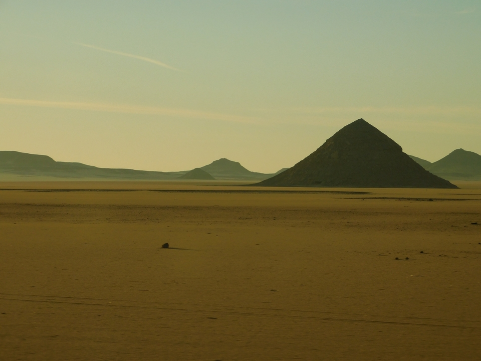 Paysage désertique sablonneux avec des collines en forme de pyramide.