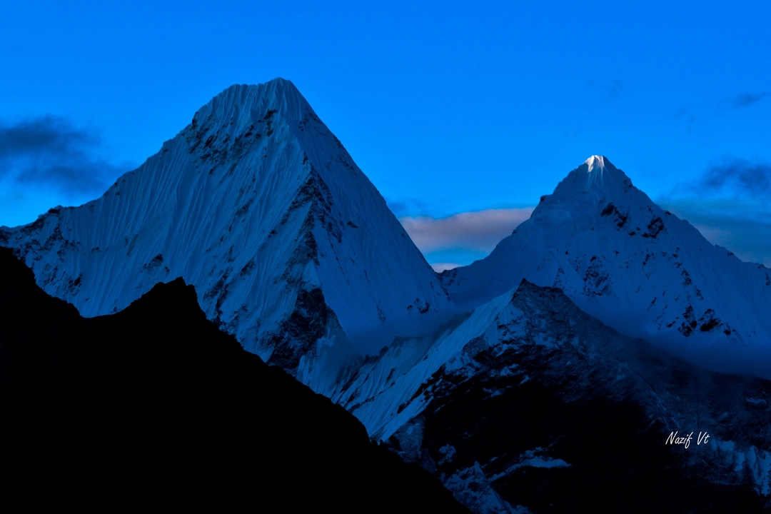 Sommets montagneux aux teintes bleues avec un ciel sombre.