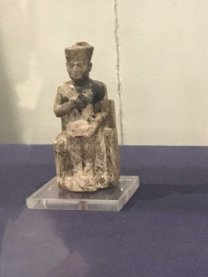 Une petite statue ancienne exposée sur un piédestal.
