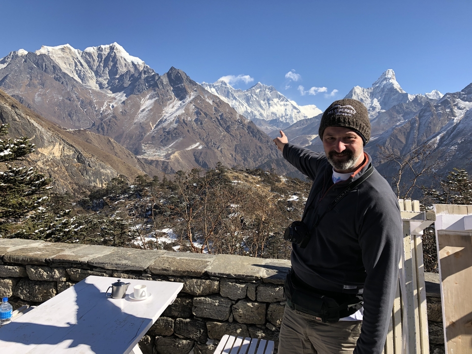 Homme pointant vers des montagnes enneigées depuis une terrasse.