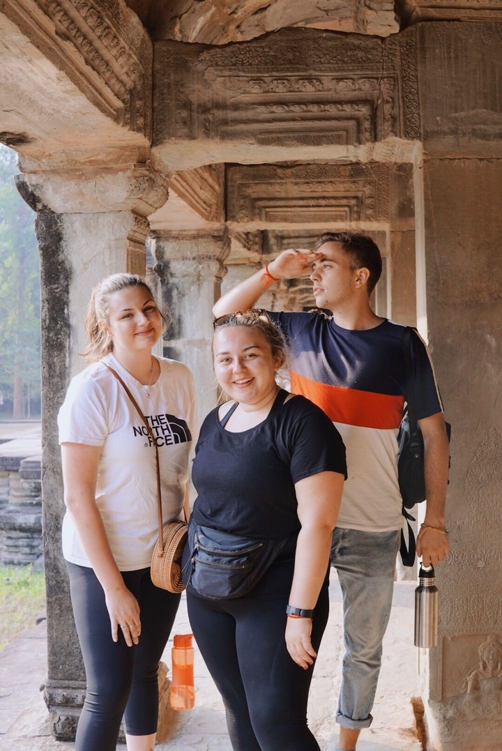 Trois personnes posent devant d'anciennes colonnes de pierre.