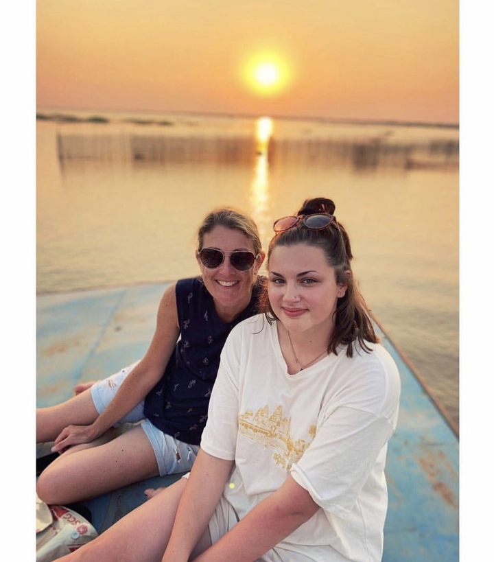 Two women smiling on a boat during sunset.