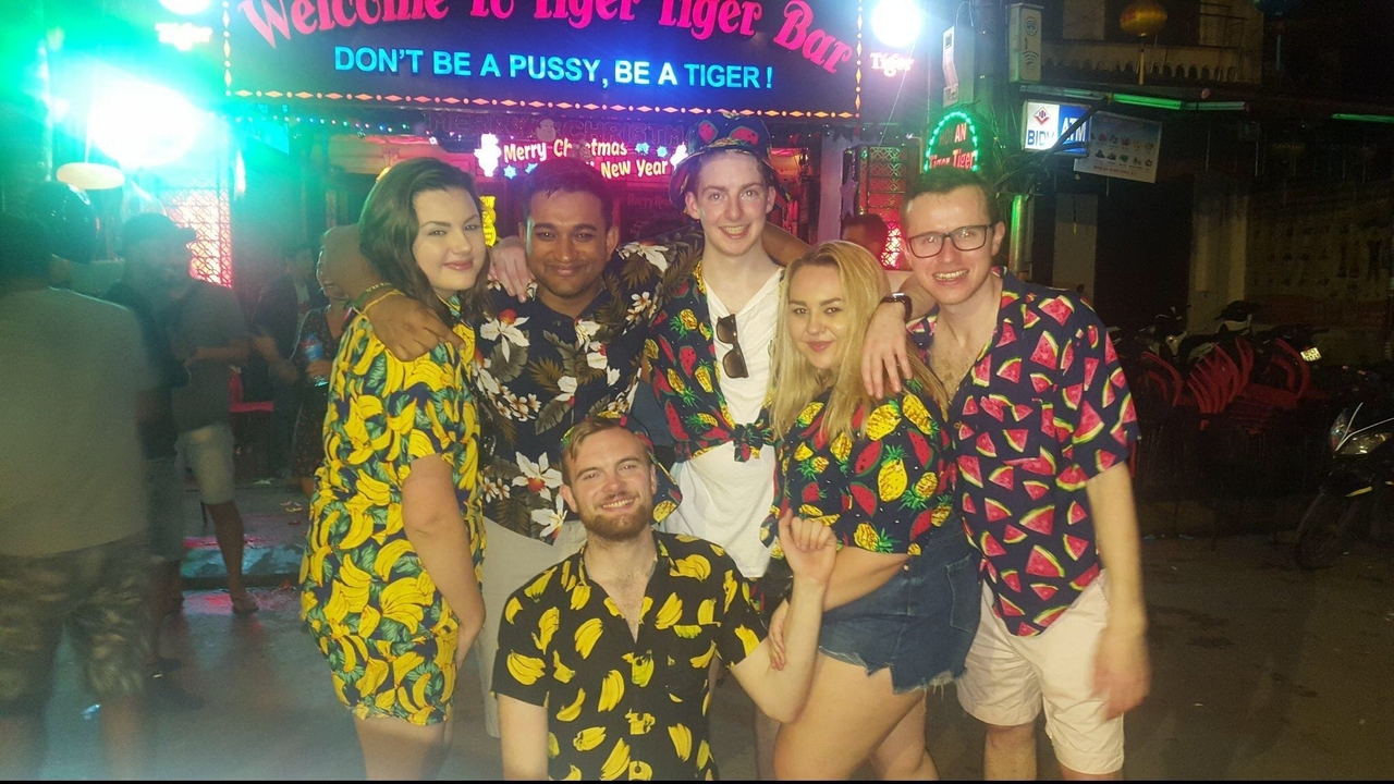 Groupe de personnes en chemises colorées posant la nuit devant une enseigne au néon.