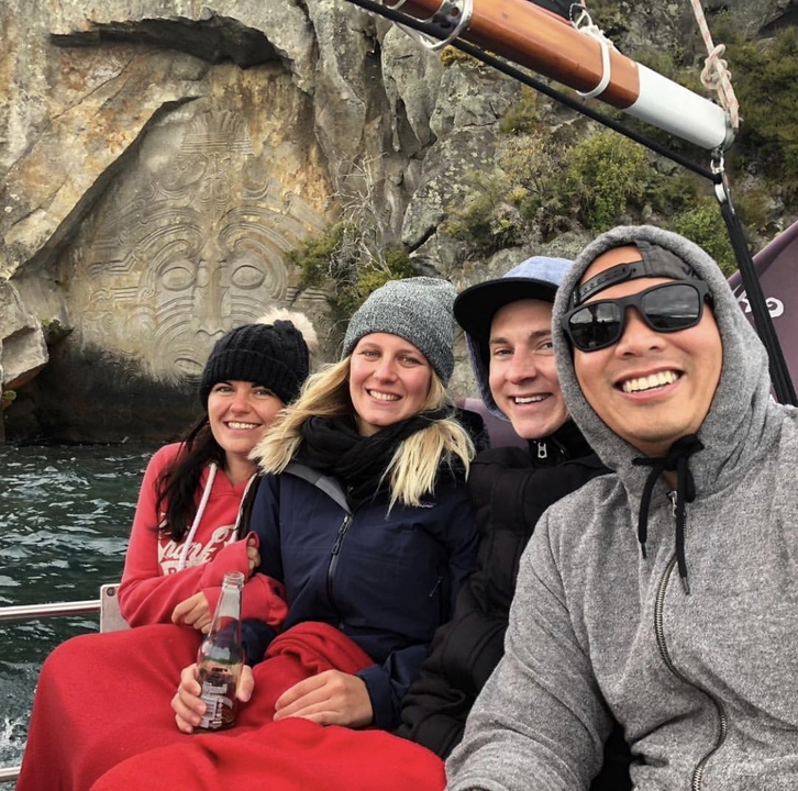 Group posing on a boat with Māori carvings nearby.