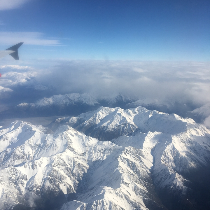 Vue aérienne de sommets montagneux enneigés sous un ciel nuageux.
