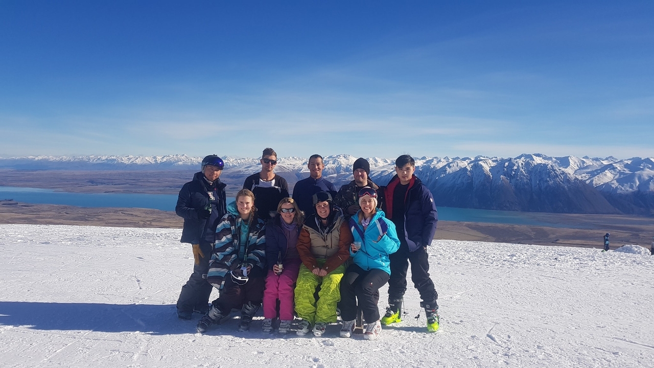 Groupe de skieurs posant avec un lac de montagne enneigé en arrière-plan.