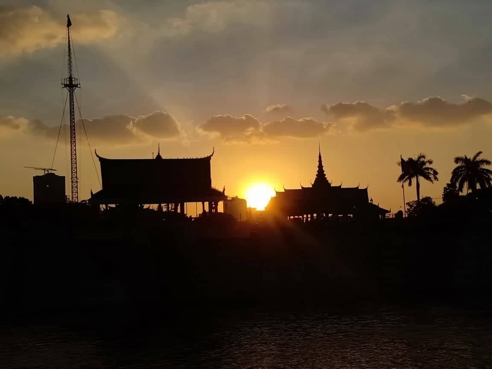 Silhouette de structures traditionnelles au coucher du soleil avec des palmiers.
