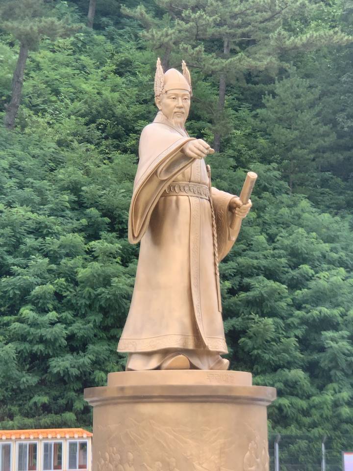 Statue d'une figure historique sur un fond de verdure.