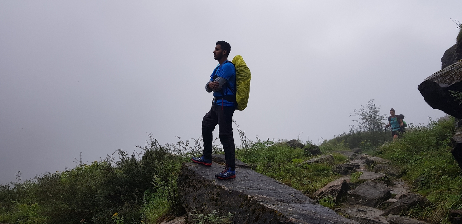 Un randonneur debout sur un sentier rocheux avec un arrière-plan brumeux.