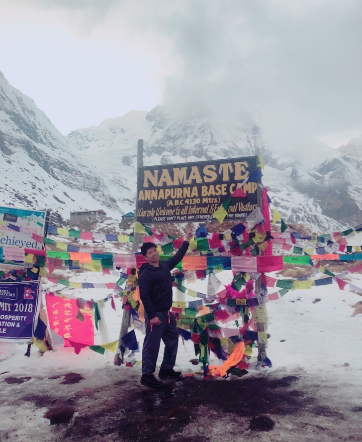 Randonneur pointant un panneau pour le camp de base d'Annapurna avec des sommets enneigés.