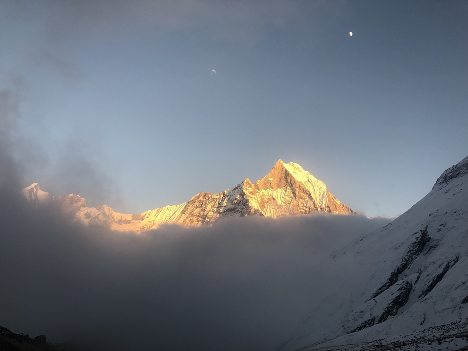 Sommet de montagne enneigé au-dessus des nuages au coucher du soleil.