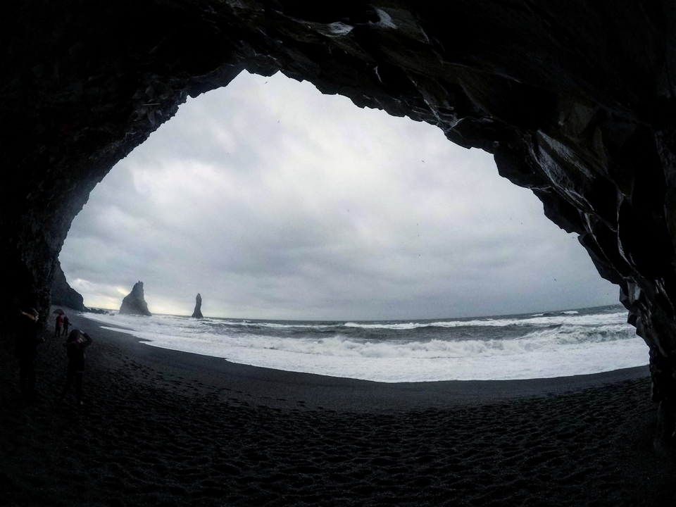 Ouverture de grotte surplombant une plage avec des aiguilles rocheuses.