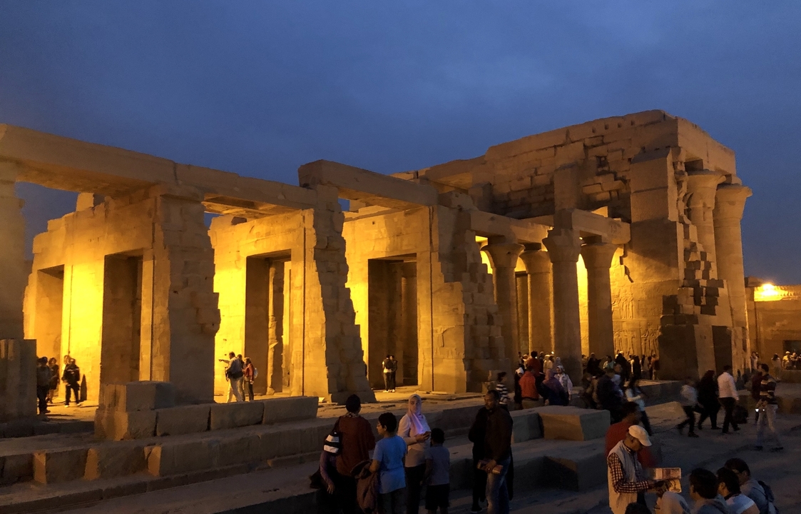 Ruines de temple bien éclairées avec de nombreux visiteurs au crépuscule.