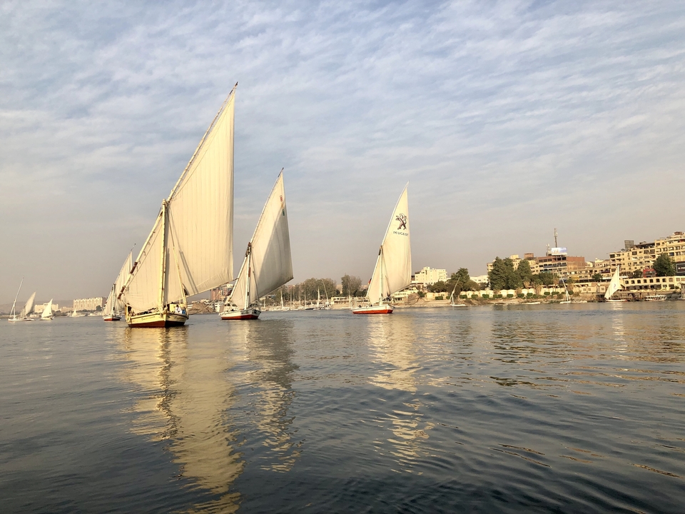 Bateaux à voile avec de grandes voiles sur une rivière sous un ciel clair.