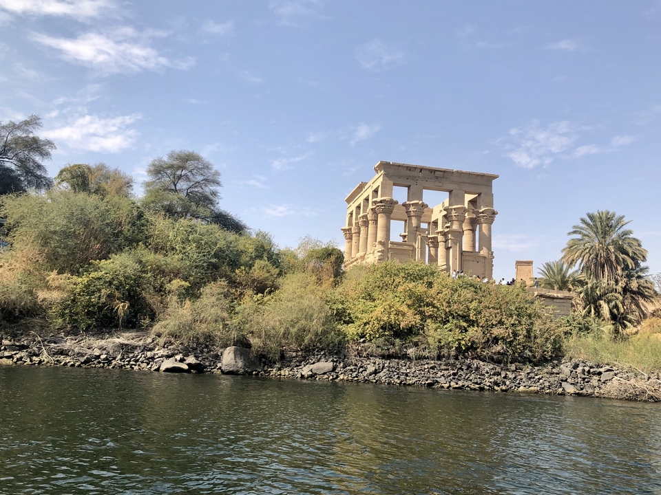 Ruines de temple antique au bord d'une rivière avec végétation.