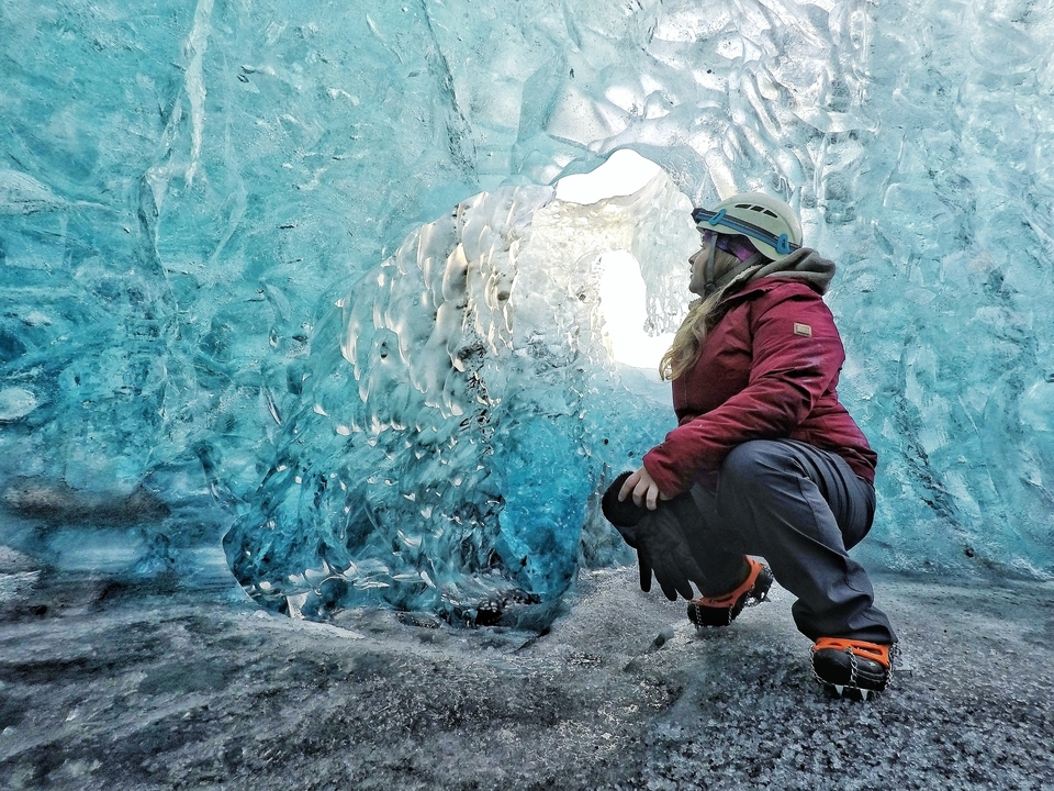 Person inside a blue ice cave wearing outdoor gear.