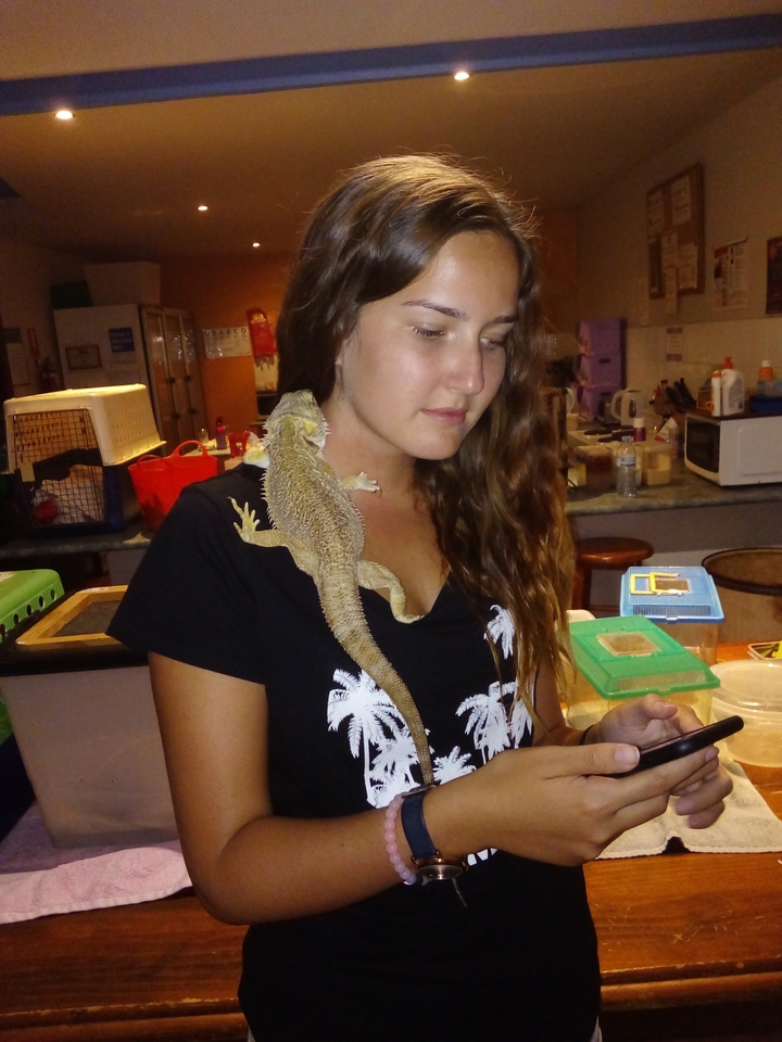 Femme aux cheveux longs tenant un reptile sur son épaule.