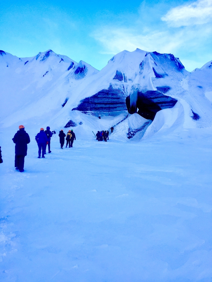 Un groupe de personnes marchant vers une grotte de glace dans des conditions enneigées.