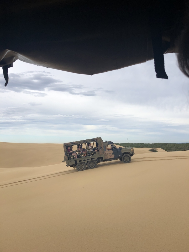 Off-road vehicle on sand dunes with passengers.