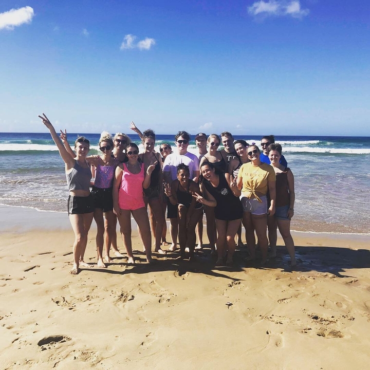 Groupe de personnes posant sur une plage avec des vagues en arrière-plan.