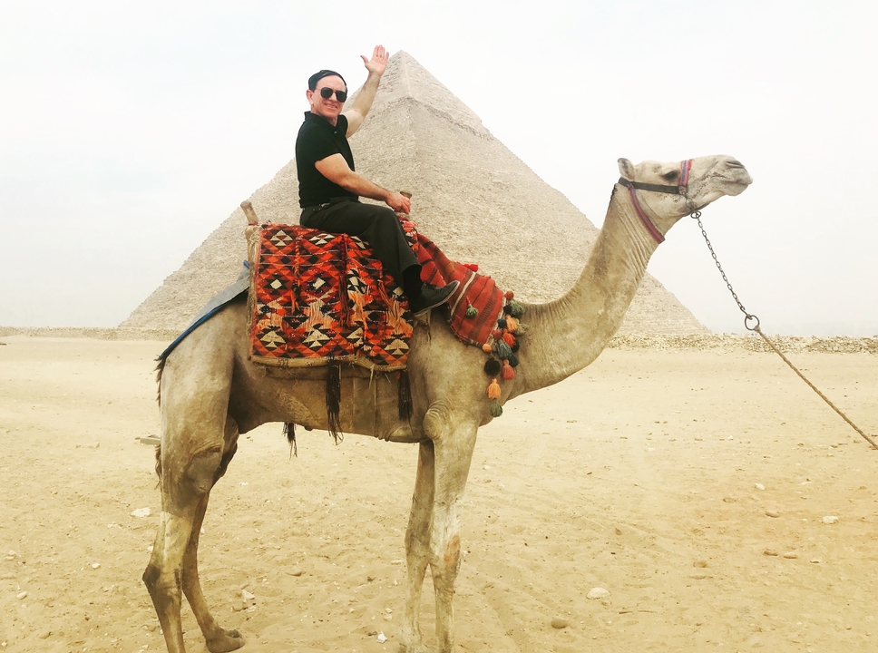 Personne à dos de chameau devant une pyramide.