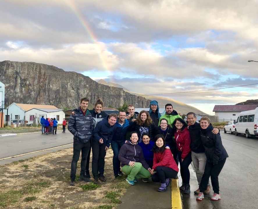 Groupe de personnes avec un arc-en-ciel au-dessus de collines rocheuses.