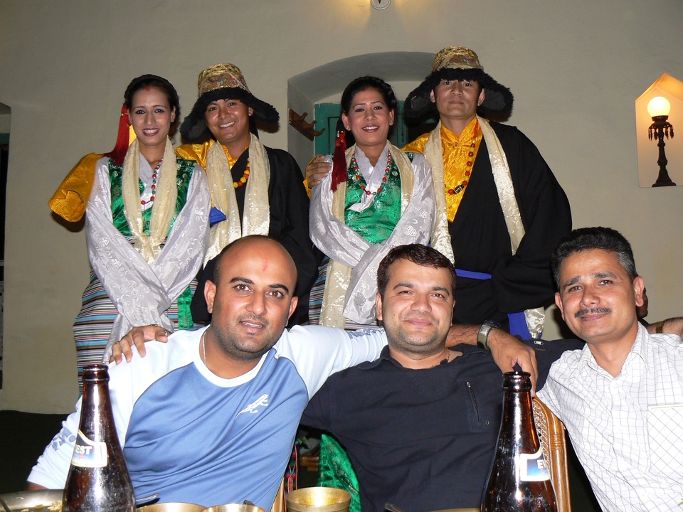 Groupe de personnes en tenue traditionnelle posant avec des amis dans un cadre intérieur.