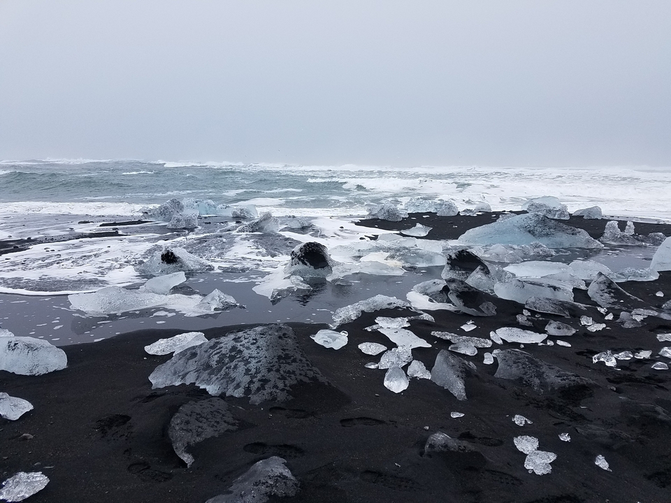 Plage de sable noir avec des blocs de glace dispersés sur le rivage.