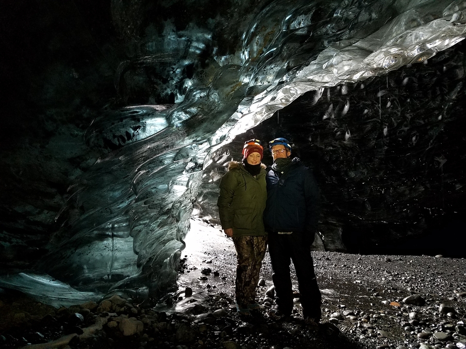 Two people standing inside an ice cave with intricate ice formations.