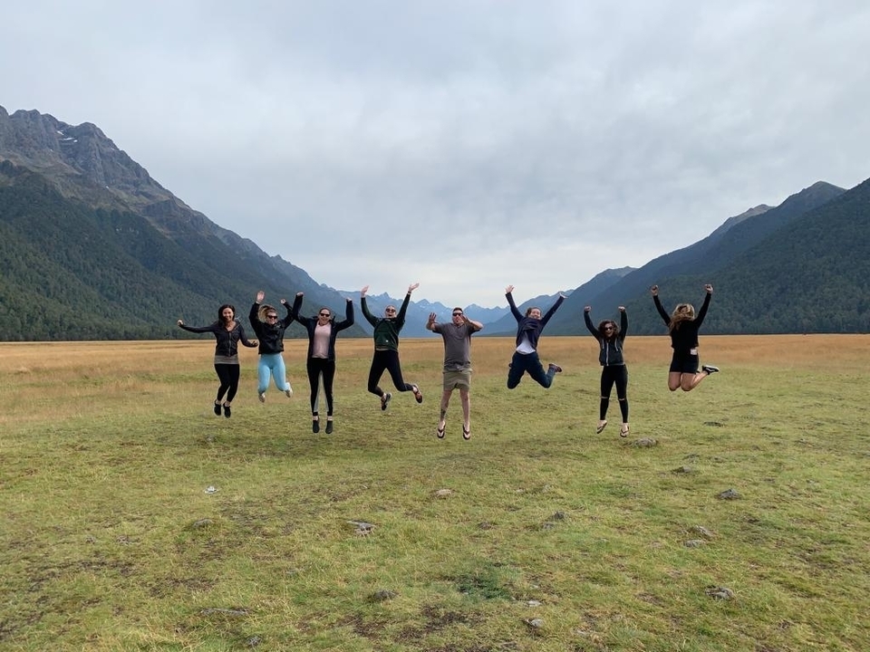 Group of people jumping in a grassy valley with mountains.