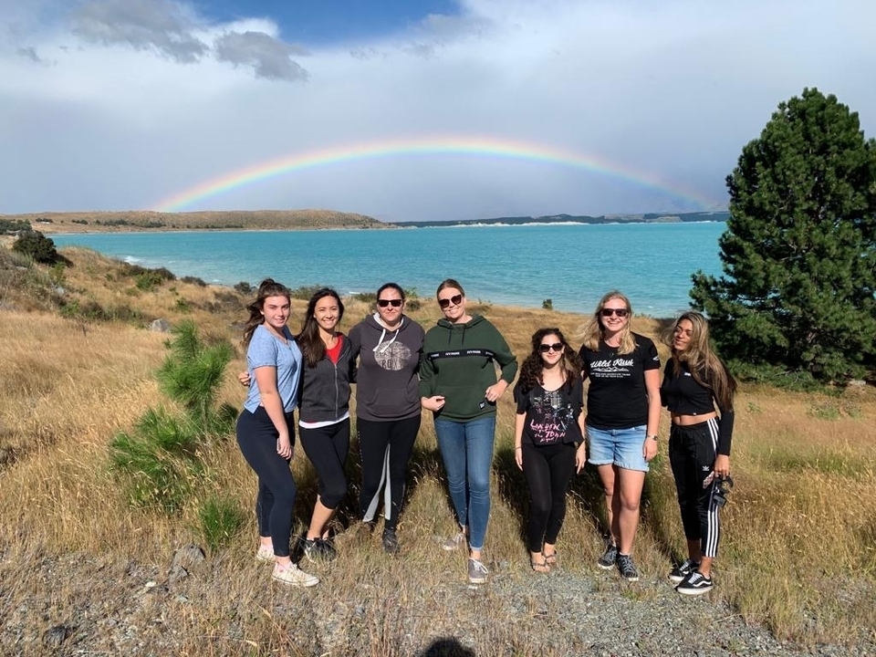Pose de groupe devant un lac avec un arc-en-ciel dans le ciel.