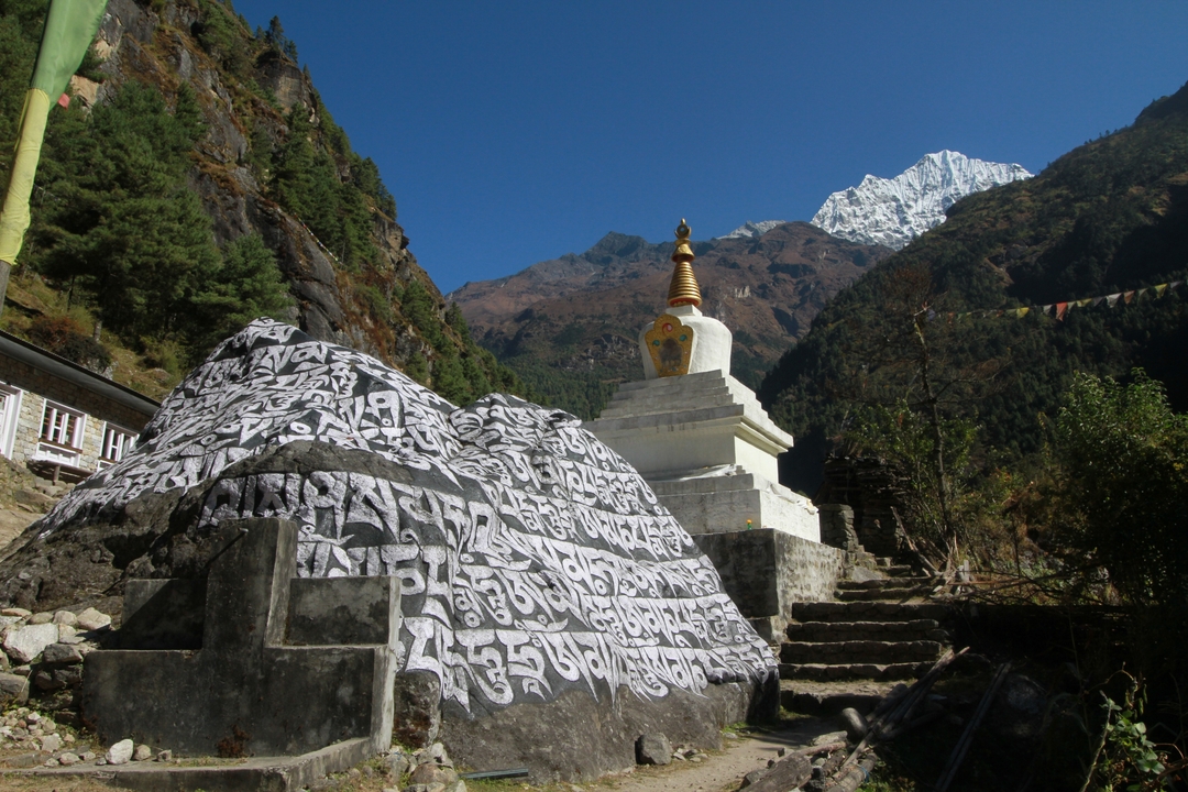 Un stupa et une roche gravée dans un paysage montagneux.