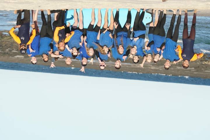 Une photo de groupe de personnes en chemises bleues et jaunes posant près de la plage.