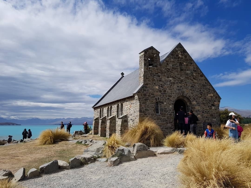 Église en pierre au bord d'un lac bleu vif avec des touristes