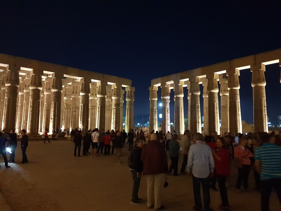 Des gens se promènent parmi des colonnes magnifiquement éclairées la nuit.