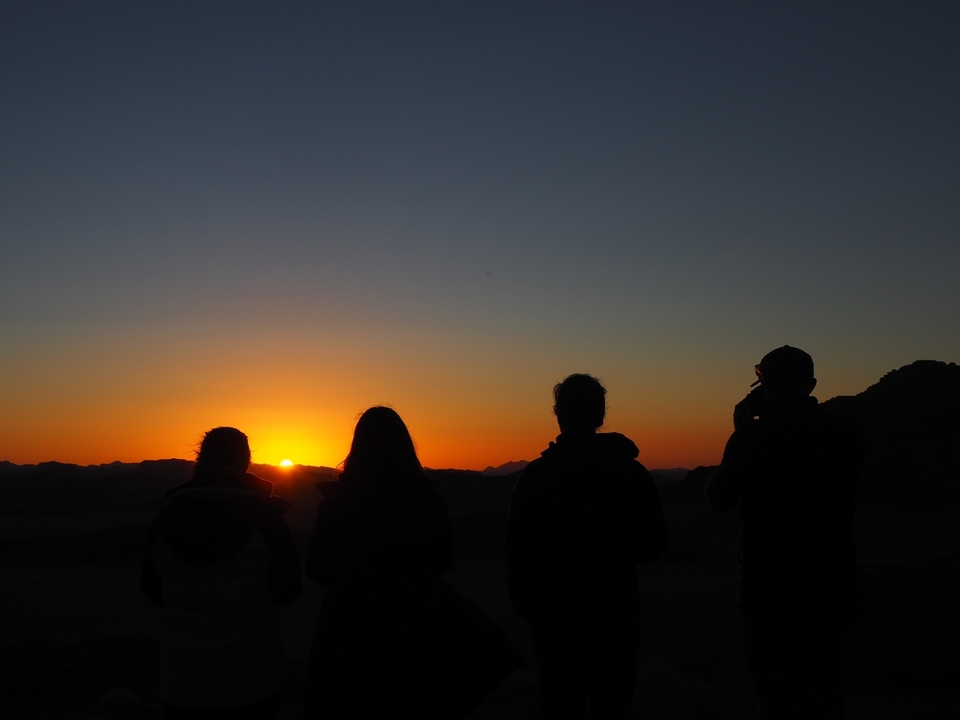 Silhouette de personnes regardant un coucher de soleil sur les montagnes.