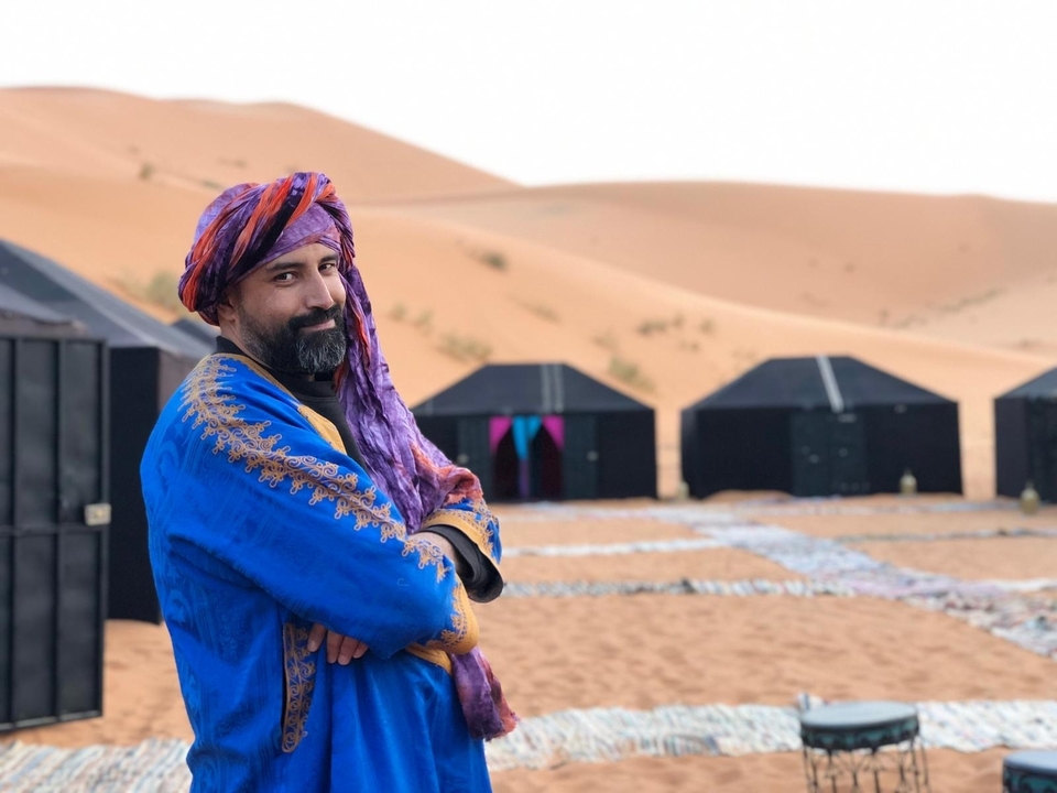 Homme en tenue traditionnelle posant dans un campement du désert.