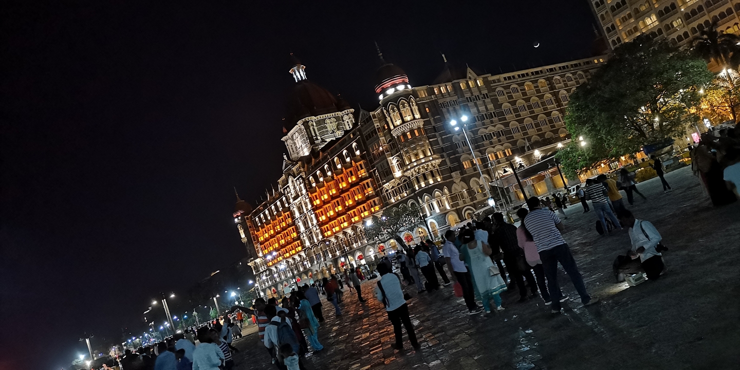 Place bondée avec des gens et un bâtiment historique éclairé la nuit.