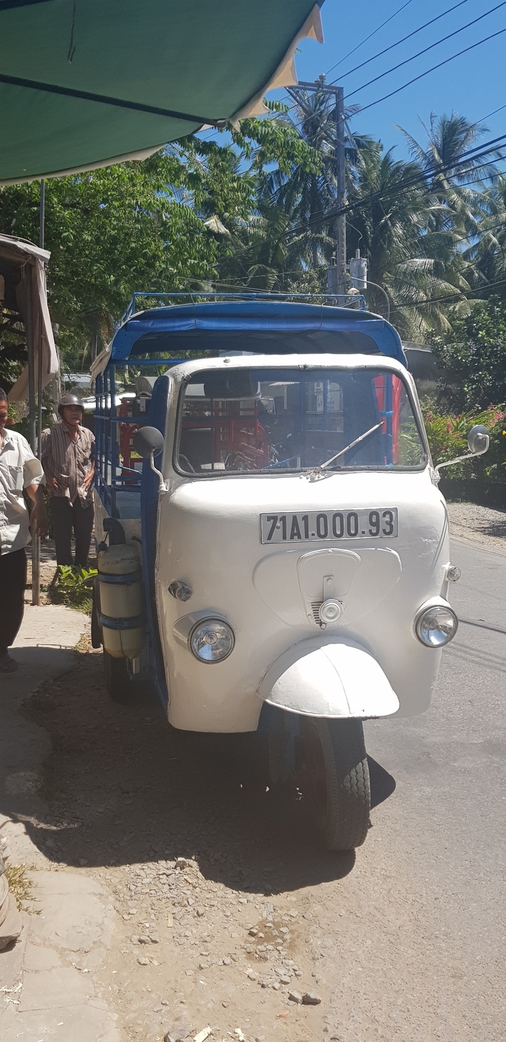 Des gens se sont rassemblés autour d'un petit véhicule blanc dans un environnement urbain.