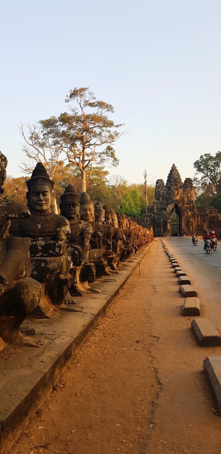 Des statues de guerriers bordent une route menant à une porte antique.