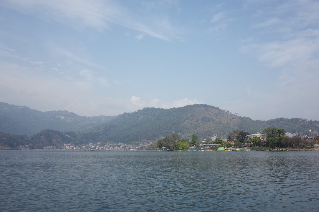 Vue d'un lac entouré de collines sous un ciel lumineux.
