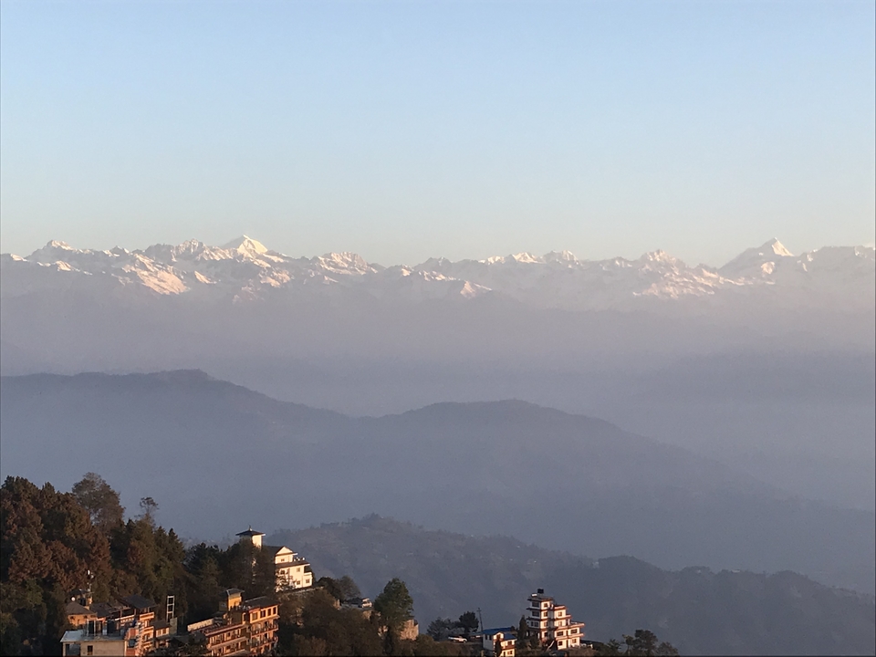 Vue panoramique des montagnes avec un petit bâtiment et des arbres au premier plan.
